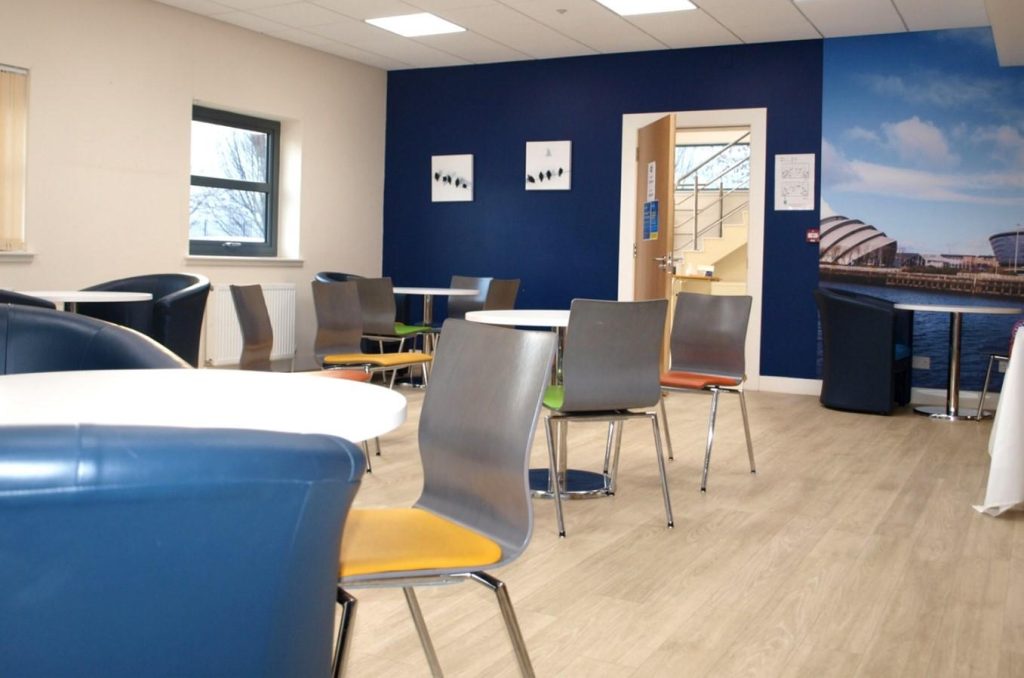 Cafe with several tables and plastic chairs. A door at the back of the room is open.
