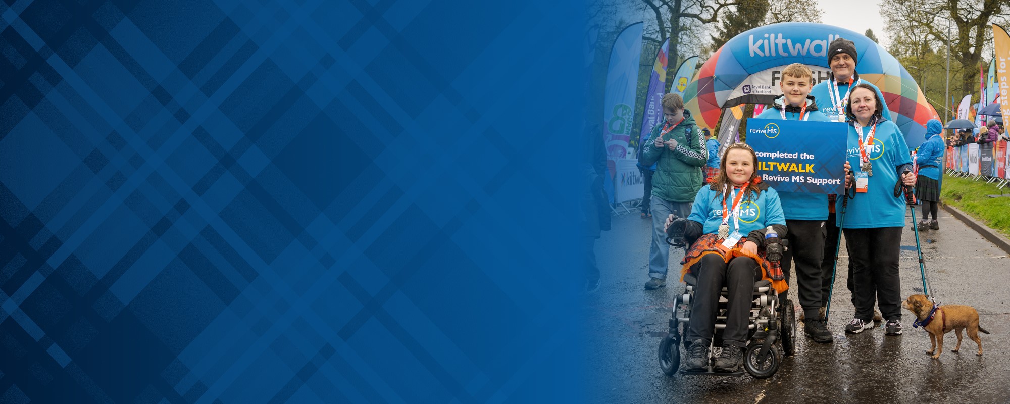 The left side of the banner image is a blue tartan. A family standing together outside at the end of a race with lots of banners in the background. There are two adults, two children and a dog. One of the children is sitting in a wheelchair.